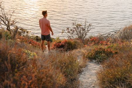 Traveller man in a T-shirt and shorts on the coast among the rocks with warm sun light.の写真素材