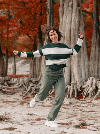 Lifestyle portrait of jumping happy woman in autumnal park. Stylish woman with emotions