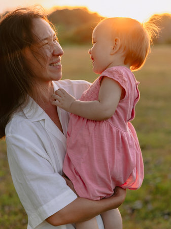 Happy mother with her cute daughter in park with warm sunset tonesの写真素材
