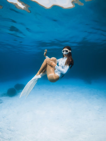 Woman with diving mack and fins in wetsuit posing in transparent clear ocean. Freediver girl posing...