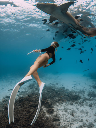 Slim woman dives in a clear tropical water with nurse sharks in Maldives