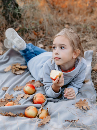 Young child girl lies on a plaid and eating apple on a picnic in parkの写真素材