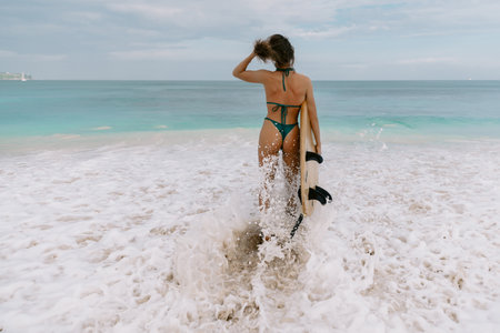 Surf girl with surfboard goes to surfing. Surfer woman in sexy bikini on ocean beachの写真素材
