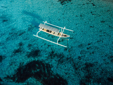 Fishing boat at anchor in blue transparent ocean on tropical island. Aerial view.