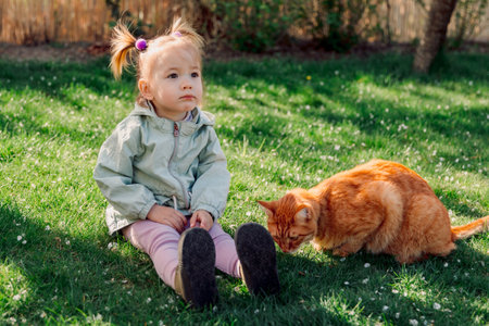 Child girl sitting with ginger cat in spring gardenの写真素材