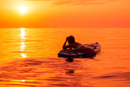 June 26, 2021. Dalaman, Turkey. Woman relaxing on stand up paddle board at quiet ocean with sunset or sunrise. Woman on Red Paddle SUP board and sunset.のeditorial素材