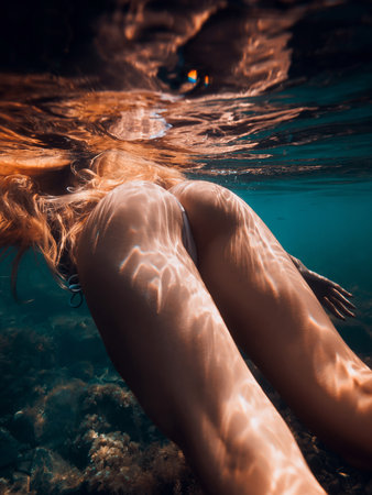 Ideal body of slim woman with red hairs underwater in sea, girl swimmingの写真素材