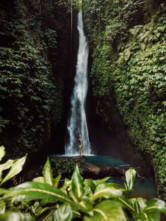 Scenic waterfall and woman in bikini. Waterfall in forest and posing traveler girlの写真素材