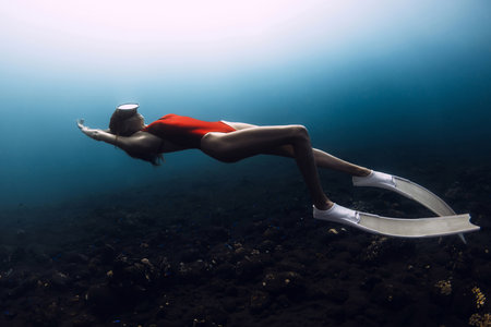 Young female freediver in red swimwear swims underwater in deep blue ocean.の写真素材