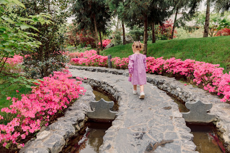 Little girl in pink dress walk in summer blooming garden with azalea flowers.の写真素材