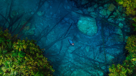 Woman floating on boat in transparent lake with crystal blue water in Indonesia. Aerial viewの写真素材