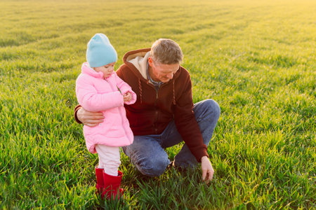 Grandfather and granddaughter walking in the field with warm sunlightの写真素材
