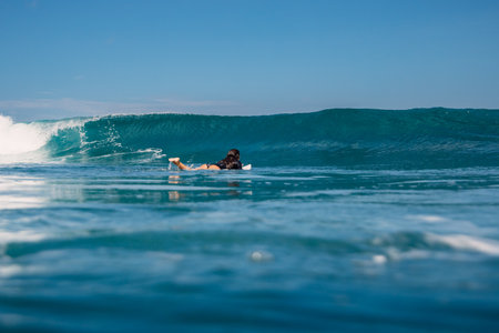 Surfer woman rowing on surfboard in ocean with crashing surfing wave.