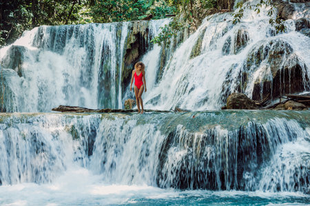 Attractive woman in red swimsuit staying on scenic cascade waterfalls in Central Sulawesiの写真素材