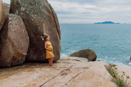 Pregnant happy woman in yellow dress posing at summer ocean coastlineの写真素材