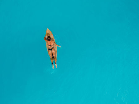 Surf girl in bikini on surfboard in blue or turquoise ocean. Drone view of surfer womanの写真素材