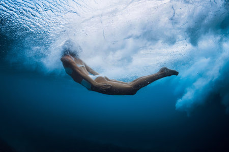 Graceful woman swimming underwater under crashing wave in crystal-clear oceanの写真素材