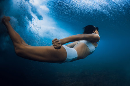 Graceful woman swimming underwater under crashing wave in crystal-clear ocean