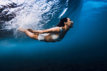 Woman swim underwater with ocean wave.