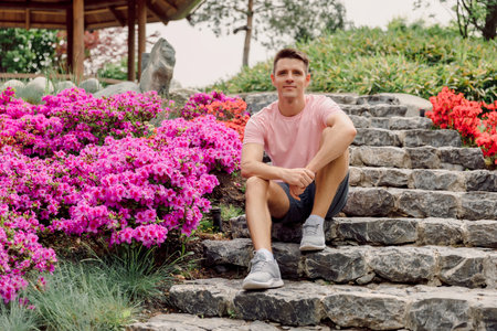 Handsome smiling man sitting on the stairs in summer garden. Caucasian male model