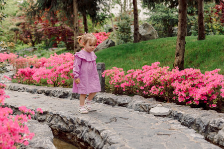 Cute child girl in pink dress walking in spring blooming gardenの写真素材
