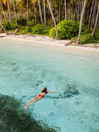 Woman swimming in tropical ocean near beach on her vacations. Aerial viewの写真素材