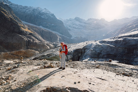 Woman hiking with backpack in the mountains. Mountains with ice glacier and touristの写真素材