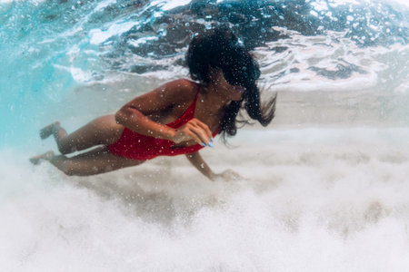 Asian woman in a red swimsuit and mask swims underwater in crystal blue tropical waters with surf waves. Soft focusの写真素材
