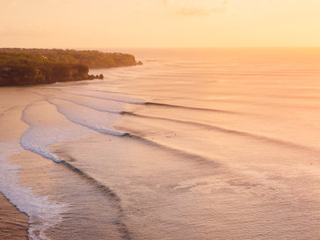 Scenic drone landscape with warm sunset tones and ocean with surfing wave in Bali.の写真素材