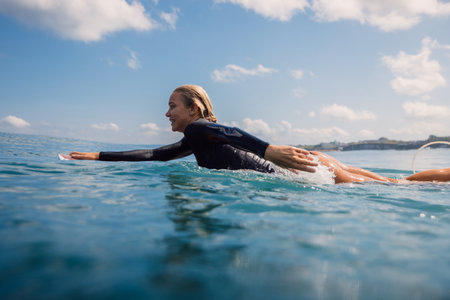 Surfer girl swims on surfboard in ocean. Woman during surfing