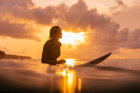 Surf girl sitting on surfboard in ocean with sunset sunlightの写真素材