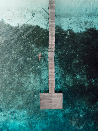 Woman swimming in tropical sea near wooden pier on her vacations. Aerial viewの写真素材