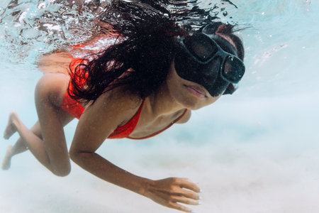 Tanned woman in a red swimsuit and mask swims underwater in tropical sea watersの写真素材