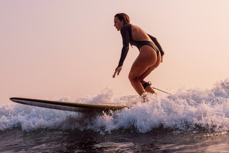 Attractive surf girl in swimsuit rides on surfboard with warm sunlight. Woman riding on longboard.の写真素材