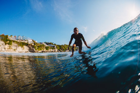 Surfer catching a wave near scenic coastline. Extreme water sport action in tropical setting