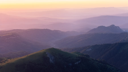 Peaceful mountain landscape at sunrise with colorful misty layers and soft golden light.の写真素材