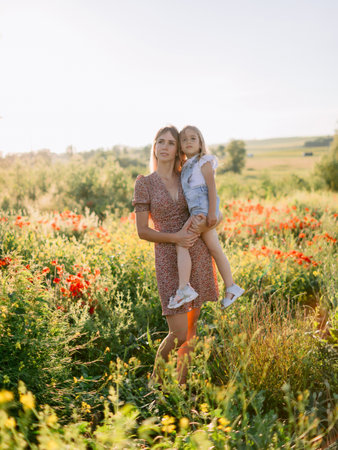 Happy mother holding daughter in blooming poppy field on a sunny summer day.の写真素材