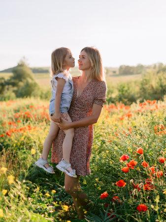 Happy mother holding daughter in blooming poppy field on a sunny summer day, enjoying nature and family loveの写真素材