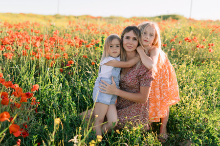 Happy mother with two daughters enjoying summer picnic in blooming poppy field. Family love concept.の写真素材