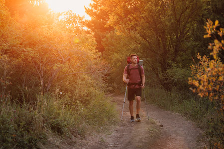 Hiker trekking through forest path with backpack and poles at sunset. Active lifestyle and adventure hiking concept.の写真素材
