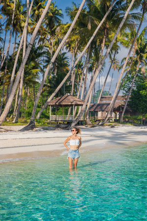 Woman on tropical beach staying in ocean on her vacations. Woman and palm treesの写真素材