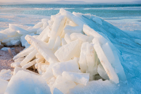 Frozen sea shoreline with stacked ice slabs at sunset, creating a surreal winter landscape of broken...