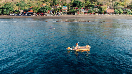 Woman kayaking in ocean on transparent kayak near coastline. Drone view