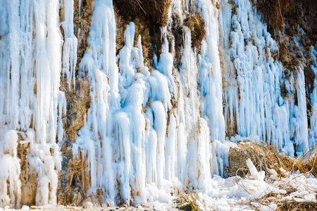 Majestic frozen waterfall with long icicles on a rocky cliff in winter.の写真素材