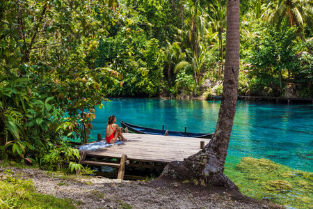 Woman in a red swimsuit sitting on a wooden pier by a turquoise lake in tropical nature.