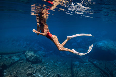 Slim woman with diving fins swims in crystal transparent water in sunny dayの写真素材