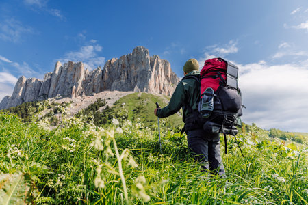 Hiker with trekking poles, backpack and solar panel in green meadow with Bolshoy Tkhach mountainの写真素材