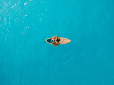Surf girl in bikini sitting on surfboard in blue ocean. Aerial viewの写真素材
