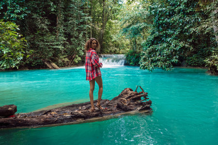 Woman standing on a log over a turquoise river in the jungle with a waterfall. Tropical adventure in Sulawesi.の写真素材