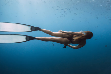 Woman freediving underwater with long fins, exploring deep blue ocean and marine lifeの写真素材